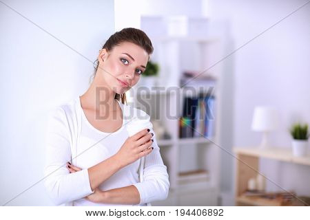 Young woman drinking cup coffee near wall