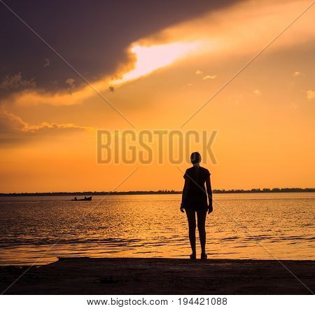 A young woman looks at the boat sailing along the estuary boat the sun will soon sit beautiful evening bright sky