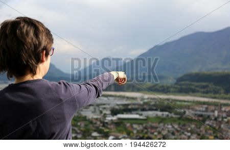 young boy pointing to the underlying panorama of the valley with a town and a river