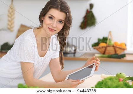 Young  woman looking for a new recipe for  cooking in a kitchen. Housewife is making online shopping by tablet computer and credit card.