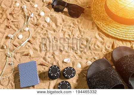 Beachpoker. Chips and cards on the sand. Around the seashells, sunglasses and flip flops. Top view. Copy space. Flat lay. Sun flare