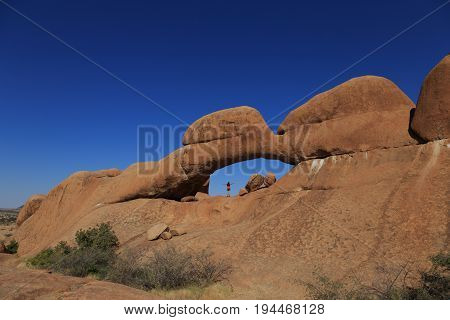 Young Girl At Stone Arch Of Spitzkoppe. Concept Of Extreme And Ecological Tourism. Natural Group Of