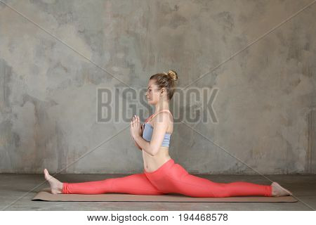 Young Woman Practicing Yoga Monkey King Pose, Hanumanasana Against Texturized Wall / Urban Backgroun