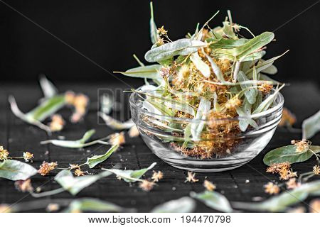 Dried linden flowers and leaves In a transparent glass bowl on Black Background.