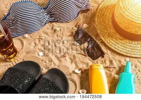 Summer bikini and accessories stylish beach set, Beach bikini summer outfit and sea sand as background, Top View, Concept. Copy space. Sun flare