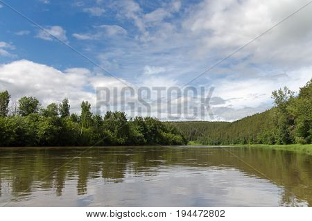 The High Water On The River Ufa In The Summer. Green Trees And Blue Sky With Clouds.