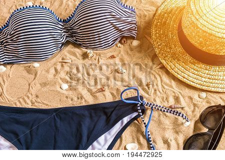 Summer bikini and accessories stylish beach set, Beach bikini summer outfit and sea sand as background, Top View, Concept. Copy space. Sun flare