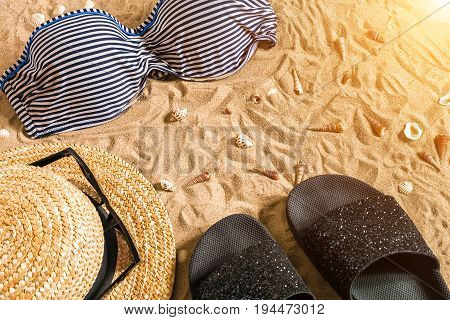 Summer bikini and accessories stylish beach set, Beach bikini summer outfit and sea sand as background, Top View, Concept. Copy space. Sun flare