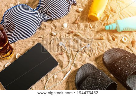 Summer bikini and accessories stylish beach set, Beach bikini summer outfit and sea sand as background, Top View, Concept. Copy space. Sun flare