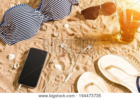Summer bikini and accessories stylish beach set, Beach bikini summer outfit and sea sand as background, Top View, Concept. Copy space. Sun flare