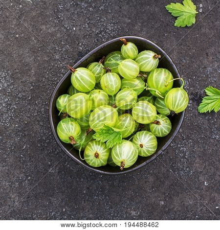 Fresh green gooseberries in a ceramic bowl on a dark background. Top view.