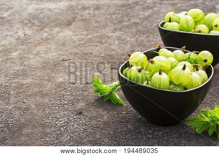 Fresh green gooseberries in a ceramic bowl on a dark background. Top view.