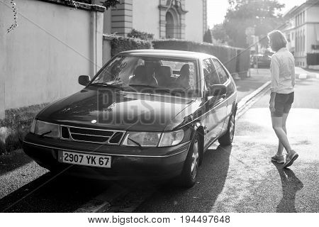 STRASBOURG FRANCE - MAY 2017: Woman walking toward her Saab 900 a compact luxury automobile which was produced by Saab from 1978 until 1998 in two generations beautiful sun flare light behind
