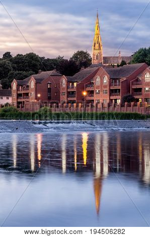 Evening view of the city of Exeter. The illuminated church of St. Leonhard. Birds are sitting on the dam.