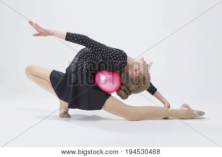 Sport Concepts. Caucasian Female Rhythmic Gymnast In Professional Competitive Black Sparkling Suit Doing Backbend Stretching Exercise With Ball in Studio On White. Horizontal Image Composition