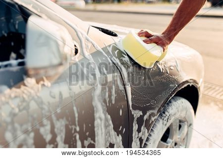 Male hand rubbing the car with foam, carwash