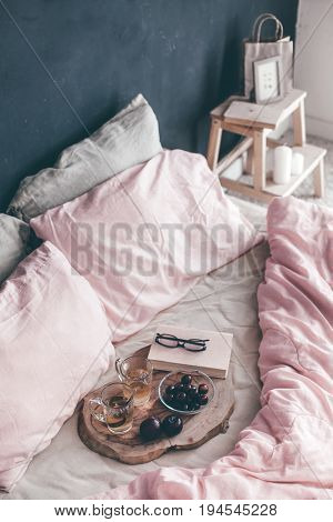 Black loft bedroom and pastel bedding set. Unmade bed with breakfast and reading on tray. Interior decor over blackboard wall. Cozy modern living space.