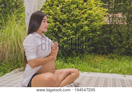Pregnant women are playing yoga in the garden.