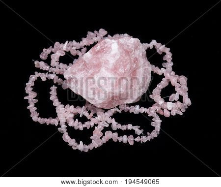 Raw rose quartz from Madagascar and polished rose quartz strings on black background