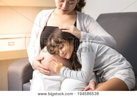 Closeup Of Happy Child Listen To Belly Of Pregnant Woman. Family Having Fun Indoor. Mothers Day Conc