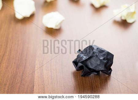 Black Crumpled Paper Ball On Dark Brown Wood Table With Group Of White Crumpled Paper Ball At Backgr