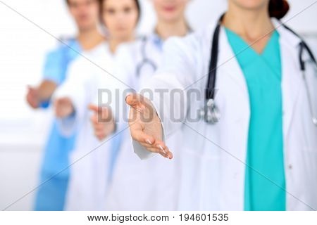 Group of doctors offering helping hand in hospital closeup. Friendly and cheerful gesture. Medical cure and tests advertisement concept. Physicians ready to examine and save patient.
