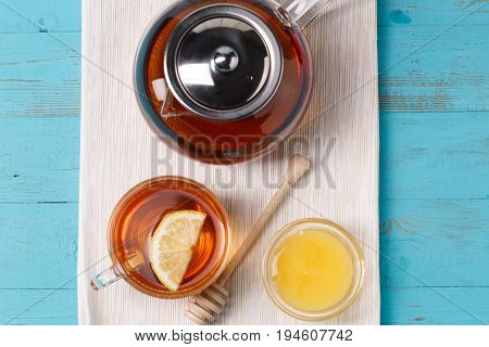 Glass cup of tea with lemon, glass teapot and honey on blue wooden table.