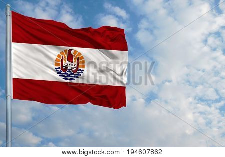 National flag of French Polynesia on a flagpole in front of blue sky.