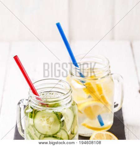Two mugs of infused detox diet refreshing waters: with cucumber and lemon on white wooden table