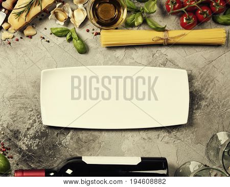 Italian food background with ravioli, vine tomatoes, basil, spaghetti, spinach, onion, parmesan, olive oil, garlic, peppercorns, rosemary and wine. Slate background 