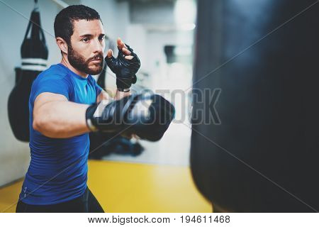 Concept of a healthy lifestyle.Young muscular man fighter practicing kicks with punching bag.Kick boxer boxing as exercise for the fight.Boxer hits punching bag.Horizontal