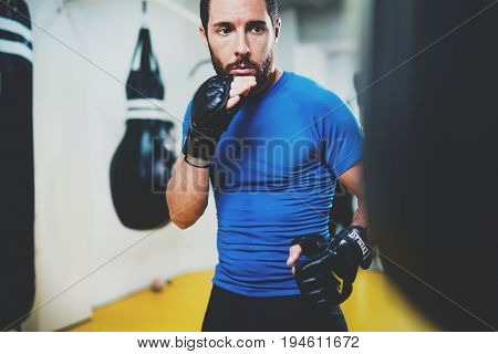 Concept of a healthy lifestyle.Young muscular man fighter practicing kicks with punching black bag.Kick boxer boxing as exercise for the fight.Boxer hits punching bag in gym.Horizontal
