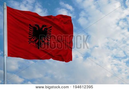 National flag of Albania on a flagpole in front of blue sky.