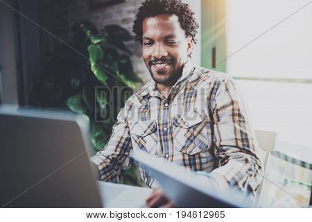 Smiling African American man using laptop while sitting in living room.Concept of young guy using Internet-enabled electronic device indoor.Blurred background.Flares