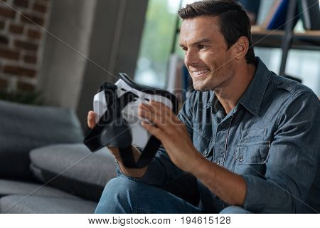 Studying new technologies. Enthusiastic handsome thoughtful guy sitting in the living room and learning about the functions of the device for exploring virtual reality