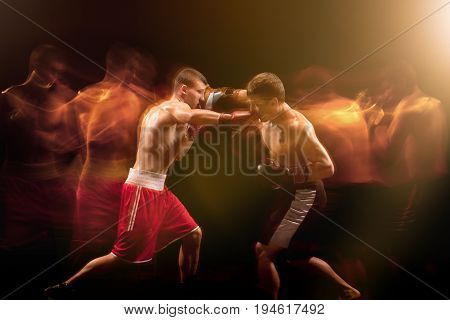 The two male athlete boxers punching with dramatic edgy lighting in a dark studio. Image made with stroboscope