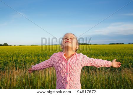 a little girl with extended arms in front of a canola field