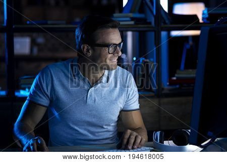 Happy with his job. Handsome persistent nice guy staying in the office till late night while working on important analysis and typing it on his computer
