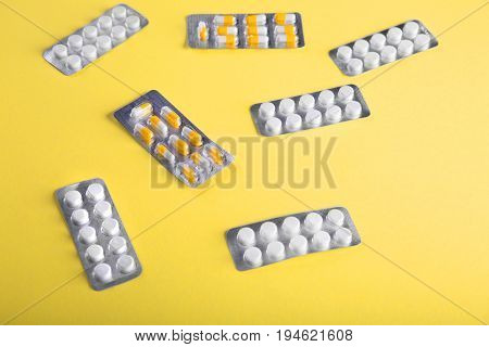 Close-up of medication on a bright yellow background. Tablets in blisters: painkillers, antibiotics, vitamins, drugs, aspirin and other.  Pharmaceutical medicament, care in container for health.