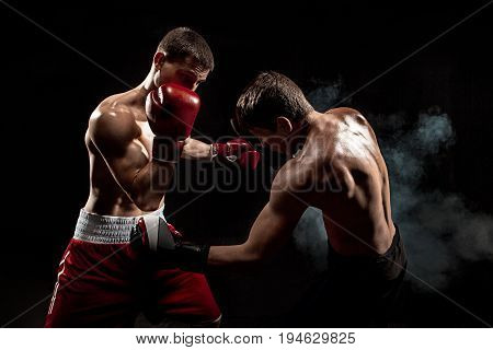 Two professional boxer boxing on black smoky studio background.