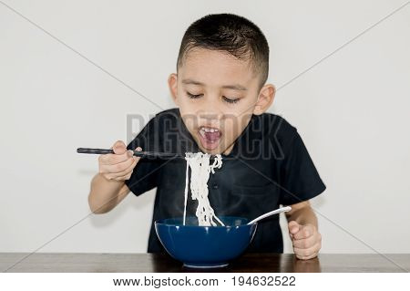 Asian boy wearing a black shirt is using chopsticks noodles in a blue ceramic cup and cooled to eat-Fast food & Beverage concepts.