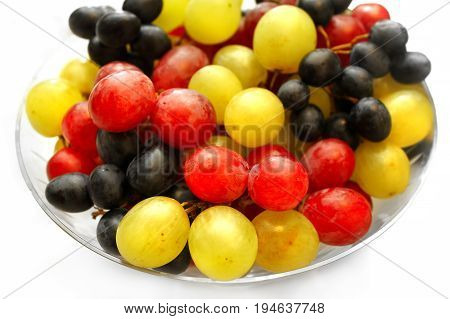 Close up of bright assortment tasty ripe grapes in a glass plate on white background