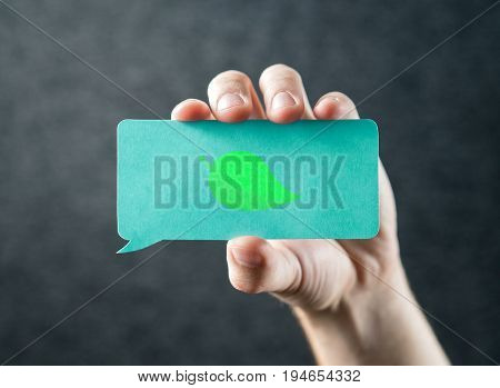 Sustainable development, eco friendly, global warming, climate change, nature protection and greenhouse effect concept. Hand holding cardboard speech bubble with green leaf icon.