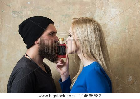 Man and woman posing with bottle of liqueur. Pretty girl with blond long hair and hipster with beard on beige background. Alcohol appetizer addictive and convive. Unhealthy lifestyle and bad habits