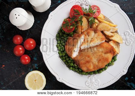 Breaded chicken breast steak with roasted potato and green peas