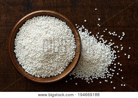 Dry Tapioca Pearls In Dark Wooden Bowl Isolated On Dark Brown Wood From Above. Spilled Tapioca.