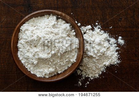 Fine White Flour In Dark Wooden Bowl Isolated On Dark Brown Wood From Above. Spilled Flour.