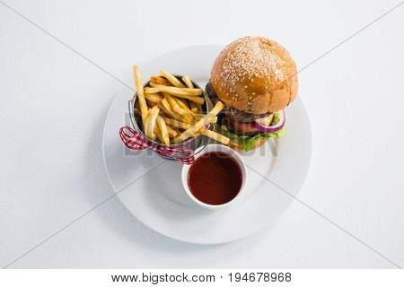 High angle view of burger by french fries in container with tomato sauce on plate against white backgroun