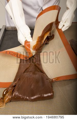 Artisanal production of caramel toffee sweets butterscotch candies. Woman with white lab coat blouse stretching moving extending the sugar pastry to do butterscotch candies sweet of France