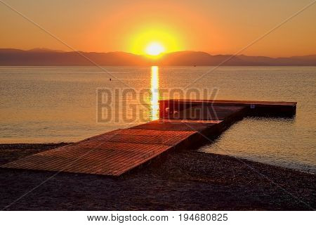 View on the sunrise on the sea the mountains and a wooden pier on the beach Moraitika island Corfu Greece.